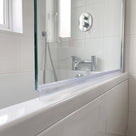 Clear tapered seal along the bottom edge of a glass bath screen in a white tiled bathroom