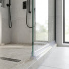 Clear tapered seal along the bottom edge of a walk-in shower screen, fin meeting a grey tiled floor