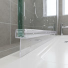 Clear tapered seal on the bottom edge of a water-flecked glass screen over a white bath, grey tiles behind