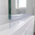 Clear tapered seal along a glass bath screen edge, fin resting on a white bath rim, white tiles behind