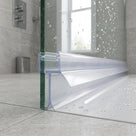 Clear seal along the foot of a wet glass shower screen on a white tray, grey tiled bathroom behind