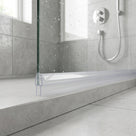 Clear seal along the bottom of a glass shower panel on a stone step, wet glass and shower hose behind
