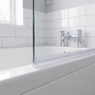 Clear seal along a glass bath screen bottom edge on a white bath, white metro tiles and taps behind