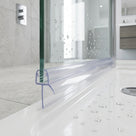 Clear seal on the bottom edge of a glass panel over a white shower tray, chrome valve and vanity behind
