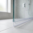 Clear seal on a glass shower panel edge reaching a pale tiled floor, chrome valve and window behind