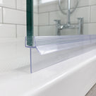 Clear seal along a glass bath screen bottom edge on a white bath, metro tiles and chrome taps behind