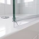 Clear seal on the bottom edge of a glass shower screen above a white tray, chrome waste behind