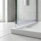 Clear seal along the bottom of a glass shower panel above a white tray, water-speckled glass