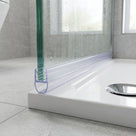 Clear seal on the foot of a green-edged glass screen over a white tray with a chrome waste, grey tiles