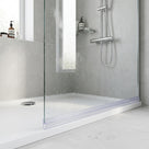 Clear seal along the foot of a wet glass screen on a low white tray, grey tiles and chrome riser behind