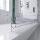 Clear seal with a bubble loop along a glass screen bottom edge on a white tray, metro tiles behind