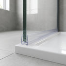 Clear seal along the bottom edge of a wet glass shower panel, sitting flat on a white tray