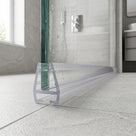 Clear deep-channel seal along the foot of a wet glass shower screen on a grey stone tiled floor