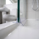 Clear seal on a glass screen bottom edge above a white bath, basin and toilet behind