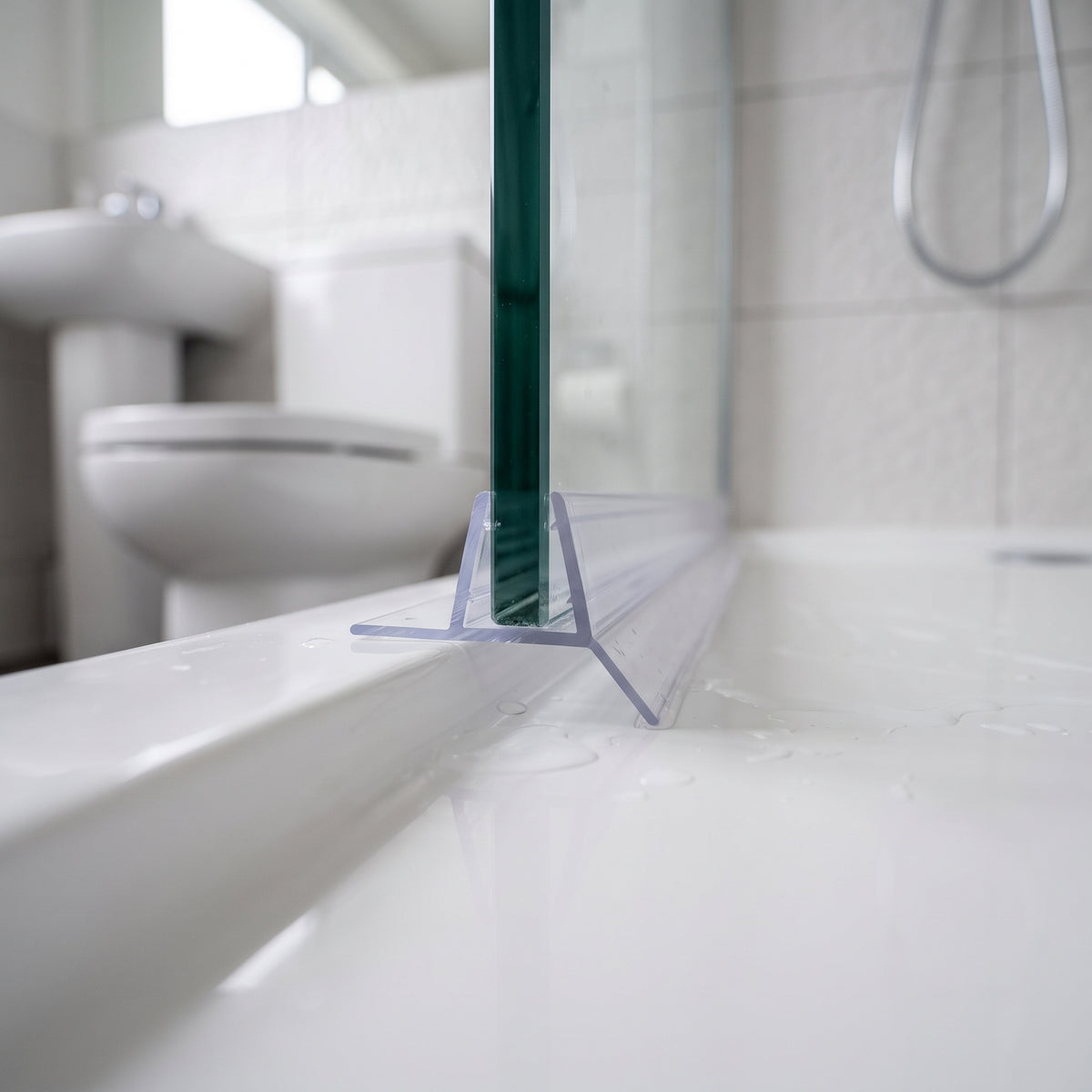 Clear seal on a glass screen bottom edge above a white bath, basin and toilet behind