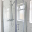 Glass shower door closed in a white-tiled bathroom, a dark vertical line down the closing edge