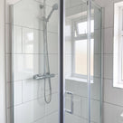 Glass shower door closed in a white-tiled bathroom, a dark vertical line down the closing edge