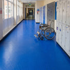 Blue small-dot vinyl matting covering a school corridor floor wall to wall beside lockers, a wheelchair parked on it