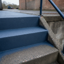 Dark blue textured step paint on external concrete steps beside a brick building and steel handrail