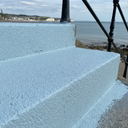 Pale blue textured step paint on seaside promenade steps, iron railings and the sea behind