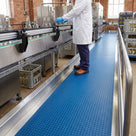 Blue penny-stud PVC matting runner along a bottling line walkway, an operative in a white coat and safety shoes standing on it