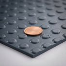 Close view of dark grey 3.3mm stud matting with a copper coin beside the studs for scale, showing each stud is about penny-sized