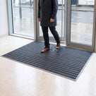 Grey entrance mat with narrow absorbent carpet inserts inside a hotel reception door, taking wet footprints from a visitor
