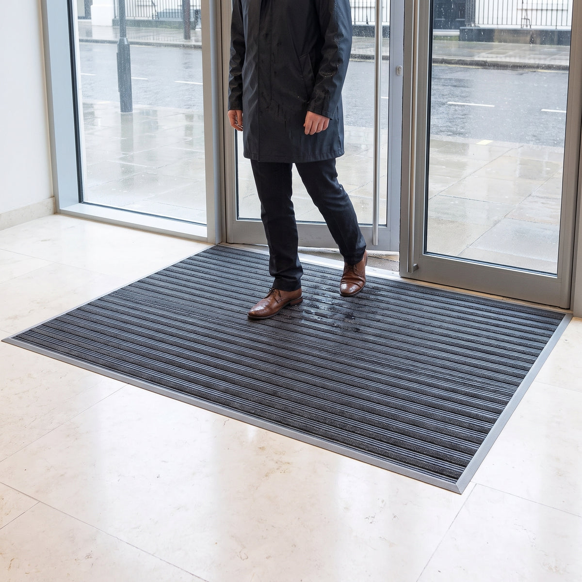 Grey entrance mat with narrow absorbent carpet inserts inside a hotel reception door, taking wet footprints from a visitor