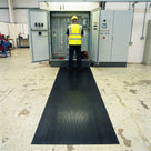 Maintenance engineer in hi-vis and safety helmet working in an open distribution board while standing on black broad-rib switchboard matting in an industrial workshop