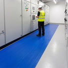 Electrician in hi-vis and safety helmet checking a motor control centre while standing on a run of blue broad-rib electrical insulation matting in a switch room