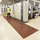 Engineer in hi-vis and safety helmet standing on brown broad-rib electrical insulation matting in front of control panels and a drive cabinet in a pump plant room