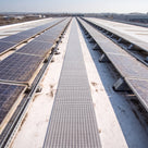 Grey open-lattice roof walkway matting loose laid as a maintenance path between rows of solar panels on a pale TPO membrane warehouse roof