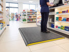 14mm dark grey pebble-embossed anti-fatigue mat with yellow foam core edge behind a retail till point