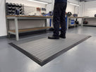 Grey ribbed anti-fatigue mat module with factory-fitted black PVC ramped edging on all four sides at an assembly workbench
