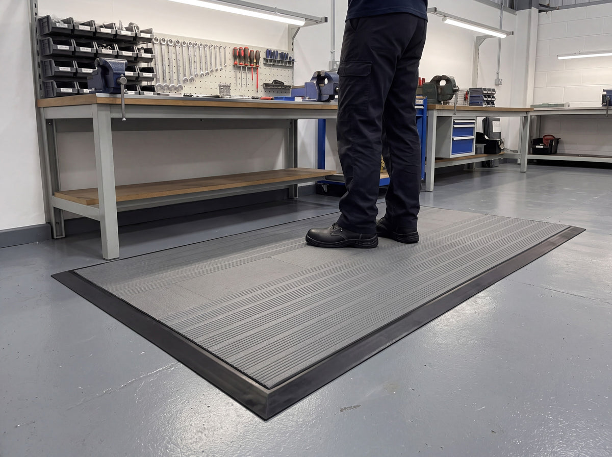 Grey ribbed anti-fatigue mat module with factory-fitted black PVC ramped edging on all four sides at an assembly workbench