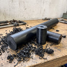 Black UHMWPE rod on a workshop bench beside two turned black rollers cut from it, black swarf around
