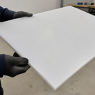 Black gloves holding a bright white panel on edge, workbenches blurred behind