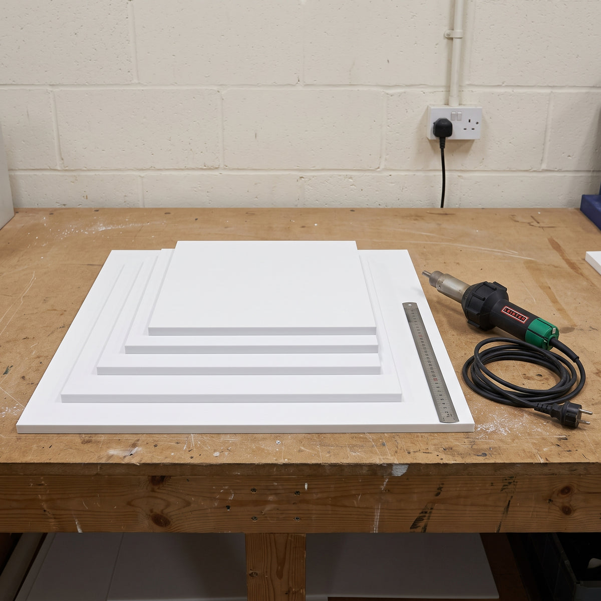 White uPVC sheets in graduated sizes stacked on a fabrication bench with a hot-air welding gun and steel rule beside them