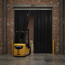 Black PVC strip curtain across a brick warehouse doorway, yellow forklift pushing through the strips