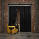 Black PVC strip curtain across a brick warehouse doorway, yellow forklift pushing through the strips