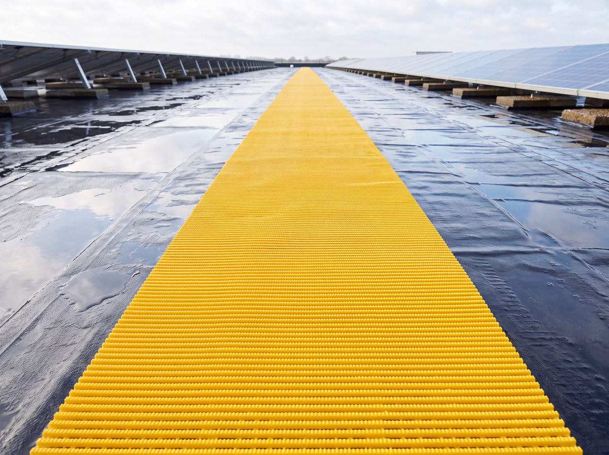 Yellow fine-rib PVC walkway matting running across a wet flat roof past solar panels