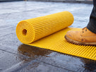 Roll of yellow fine-rib roof walkway matting being unrolled onto a wet single-ply membrane
