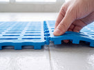 Two soft blue EVA tiles being clicked together, showing the moulded interlocking tabs, slotted top and 15mm integral feet
