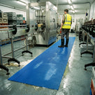 Blue open mesh PVC drainage matting along the operator walkway beside a brewery bottling line