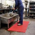 Red open mesh PVC matting used as a standing platform at an engineering workshop parts wash-down bay