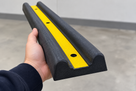 Hand holding a double-D rubber wall guard end-on, showing twin half-round ribs and yellow centre strip