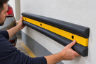 Installer holding a double-D rubber wall guard in place on a wall, countersunk fixing holes visible