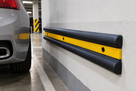 Black double-D rubber wall guard with yellow reflective strip fitted along a car park wall beside a parked car