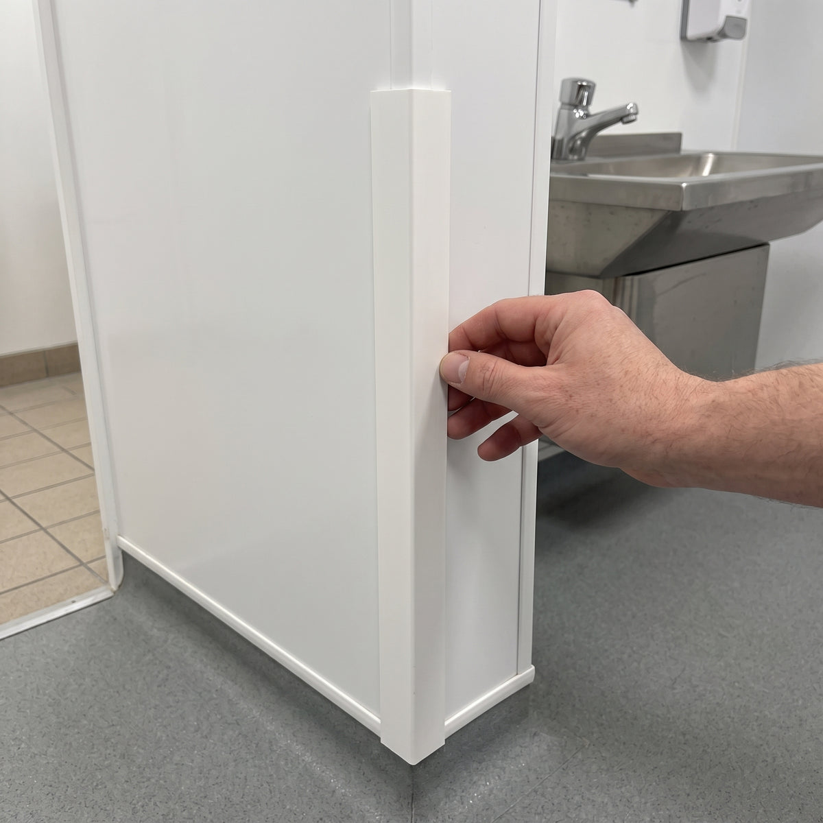 White PVC external angle fitted over the corner of white hygienic wall cladding in a washroom, hand pressing it home
