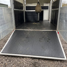 Empty horsebox with ramp lowered, floor and ramp covered in black wide rib rubber matting with hoof prints and loose hay